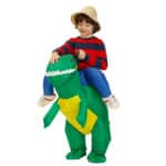 Enfant portant un déguisement de dinosaure gonflable vert qui donne l'impression qu'il est en train de le chevaucher , le petit garçon porte un chapeau couleur paille et carresse le dinosaure