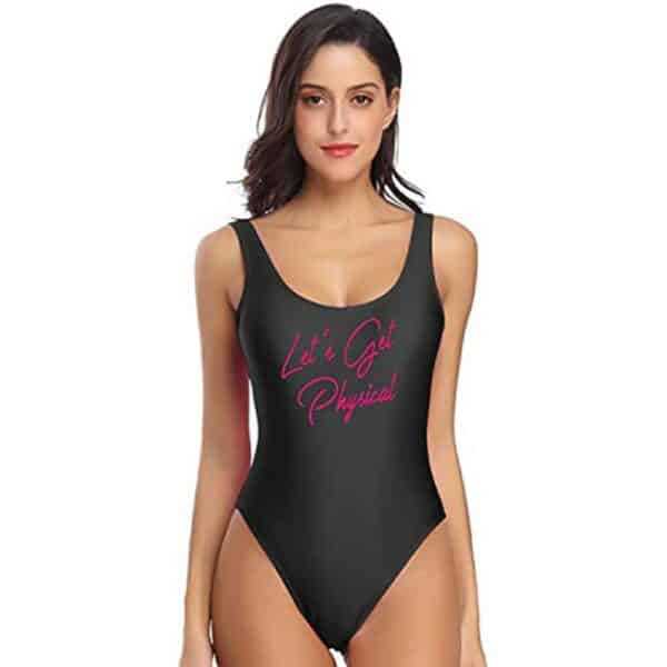 Femme brune sur fond blanc portant un maillot de bain une pièce noire avec une inscription violette au milieu du maillot