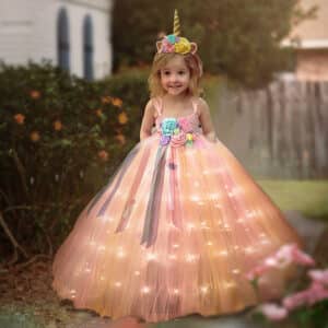 Petite fille souriante debout dans un jardin portant une robe de princesse rose lumineuse