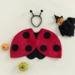 Déguisement de coccinelle pour bébé avec accessoire pour la tête des antennes de la coccinelle, sur fond beige.