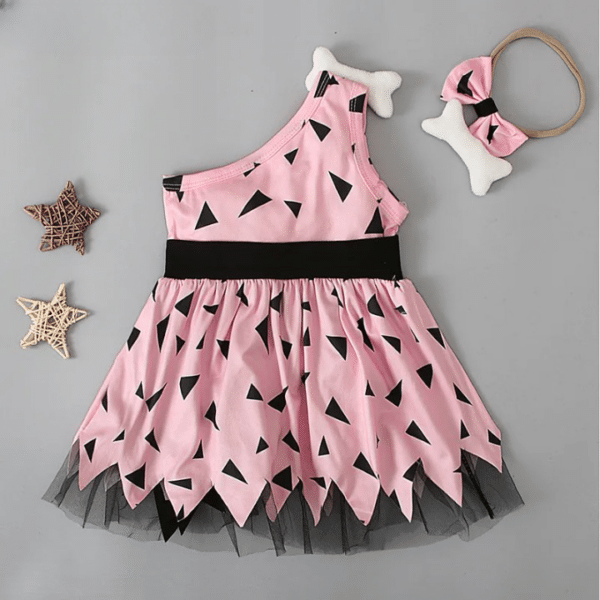 Robe de petite fille costume d'homme préhistorique rose avec des imprimé noir. La robe a un côté asymétrique, une ceinture noire et est évasée en bas. Il y a un bandeau avec un os dessus posé à côté.