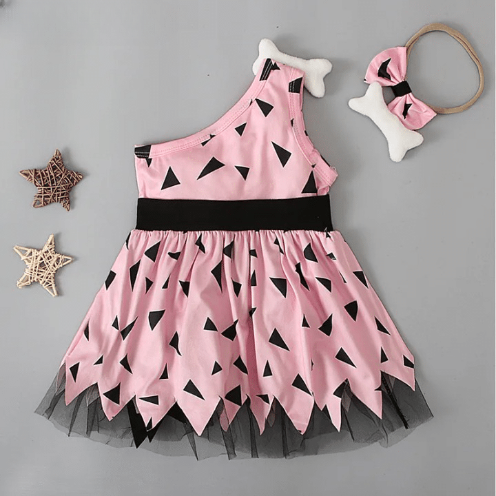 Robe de petite fille costume d'homme préhistorique rose avec des imprimé noir. La robe a un côté asymétrique, une ceinture noire et est évasée en bas. Il y a un bandeau avec un os dessus posé à côté.