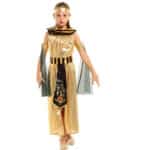 Une petite fille pose dans un déguisement de reine égyptienne. Le costume est composé d'une robe dorée ornée d'un plastron noir et doré, d'une ceinture assortie avec un pan sur lequel apparaissent des hiéroglyphes. Le costume est aussi composé de deux bracelets avec drapés noirs et d'un bandeau doré pour les cheveux.
