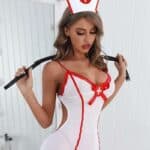 Femme aux cheveux longs portant une tenue d'infirmière sexy compsoée d'une robe moulante blanche et rouge avec un chapeau d'infirmière et un fouet derrière ses épaules.