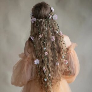Une fille pose de dos, elle montre ses longs cheveux blondes ornés d'une couronne de fleurs qui tombent en cascade sur ses cheveux.