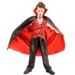 Garçon portant le costume petit vampire pour enfant qui se compose d'une chemise blanche, un gilet rouge à motifs de chauve souris, un pantalon noir et une longue cape rouge et noire, sur fond blanc.