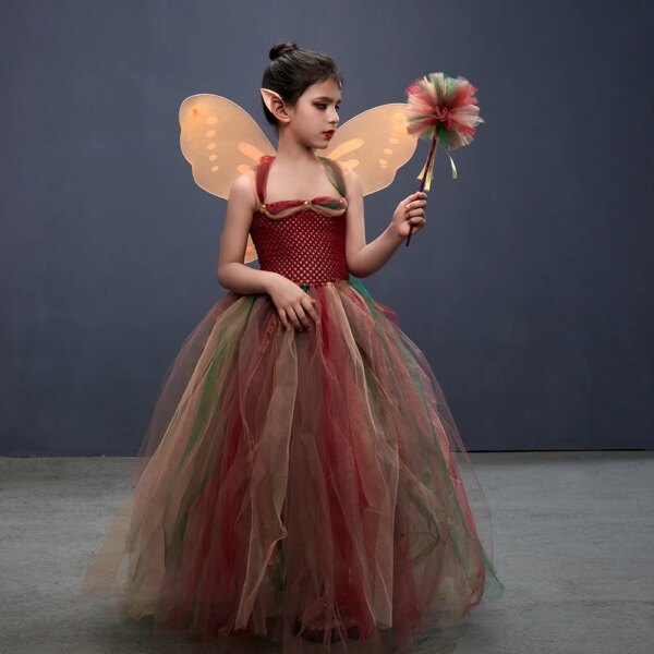 Une petite fille porte un déguisement de fée. Ce déguisement est composé d'une robe en tulle avec des couleurs de la forêt. Le costume est composé également d'une baguette, d'ailes orange et d'oreilles de fée.