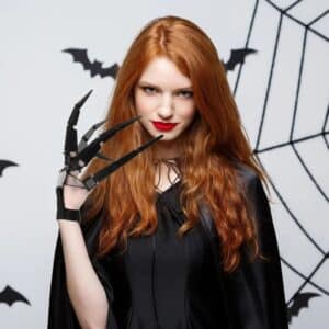 Femme déguisée pour Halloween habillée en noir avec un accessoire de main avec des doigts articulés noirs, sur fond gris