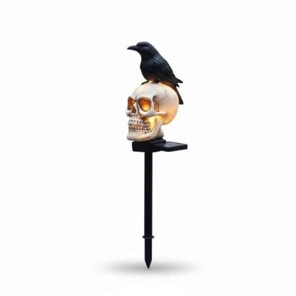 Lampe d'extérieur avec un crâne de squelette sur un piquet noir et avec un corbeau posé dessus, sur fond blanc