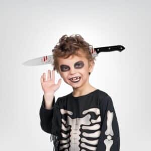 Petit garçon déguisé en squelette pour Halloween avec un serre-tête couteau sanglant, sur fond gris